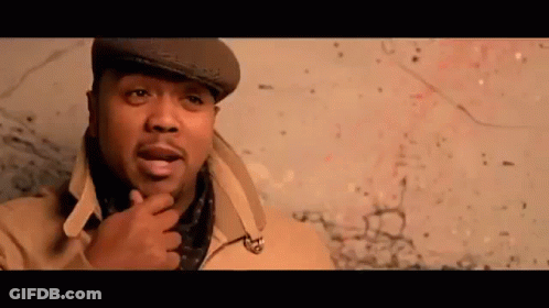 A Man Wearing A Hat And Scarf Is Standing In Front Of A Wall . GIF