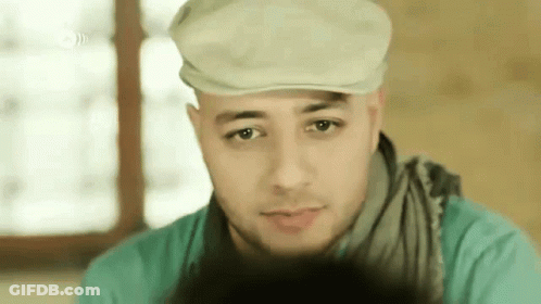 A Man Wearing A Hat And Scarf Looks At The Camera . GIF