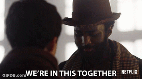 A Man Wearing A Hat And Scarf Talks To Another Man With The Words " We 'Re In This Together " Below Him GIF