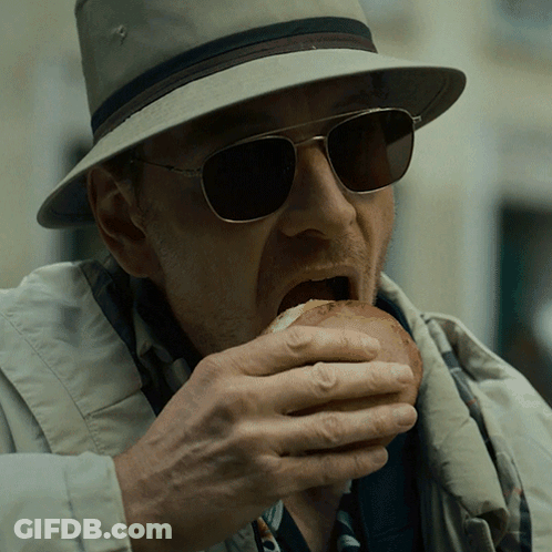 A Man Wearing A Hat And Sunglasses Eats A Sandwich GIF