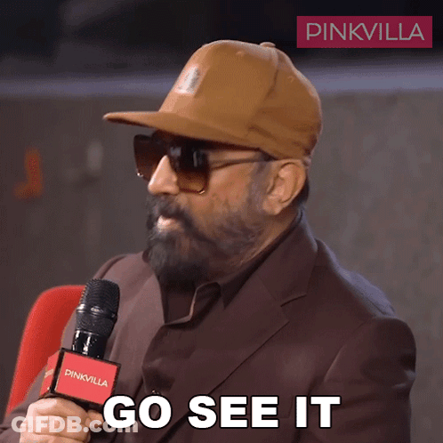 A Man Wearing A Hat And Sunglasses Is Holding A Microphone And Says Go See It GIF