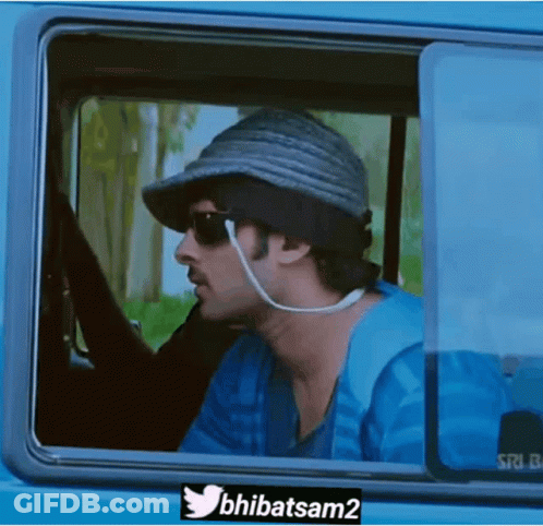 A Man Wearing A Hat And Sunglasses Is Looking Out Of A Car Window . GIF