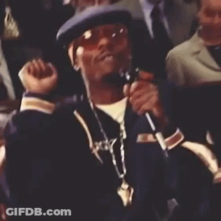 A Man Wearing A Hat And Sunglasses Is Sitting In A Crowd And Smiling . GIF