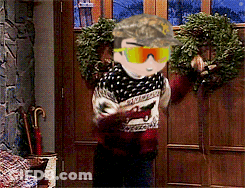 A Man Wearing A Hat And Sunglasses Is Standing In Front Of A Door With A Wreath On It GIF
