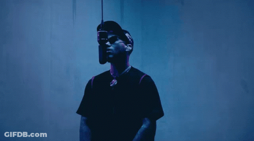 A Man Wearing A Hat And Sunglasses Is Standing In Front Of A Microphone GIF