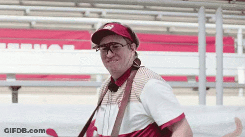 A Man Wearing A Hat And Sunglasses Is Standing In Front Of A Red And White Bench . GIF