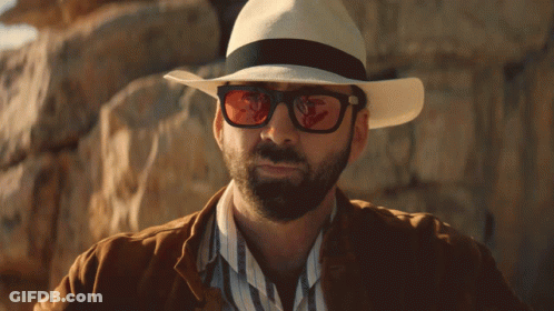 A Man Wearing A Hat And Sunglasses Is Standing In Front Of A Rock Wall GIF