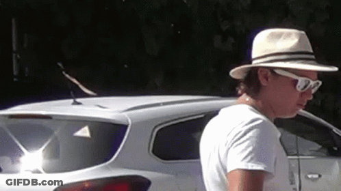 A Man Wearing A Hat And Sunglasses Is Standing In Front Of A White Suv . GIF