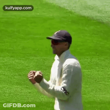 A Man Wearing A Hat And Sunglasses Is Standing On A Cricket Field . GIF