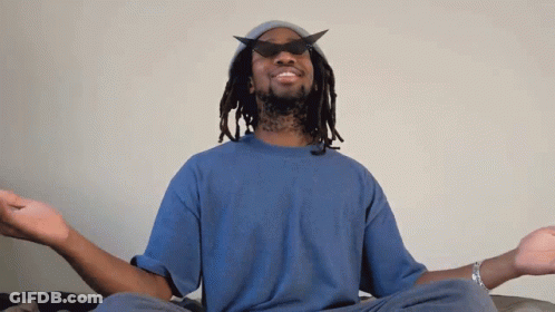 A Man Wearing A Hat And Sunglasses Sits In A Lotus Position With His Eyes Closed GIF