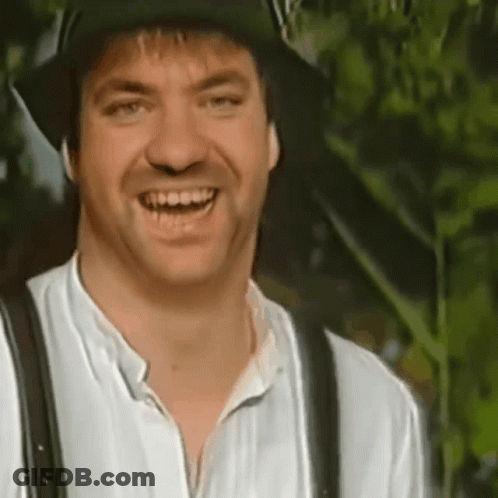 A Man Wearing A Hat And Suspenders Is Smiling And Looking At The Camera . GIF
