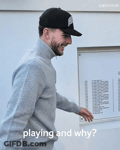 A Man Wearing A Hat And Sweater Is Standing In Front Of A Sign That Says " Playing And Why " GIF