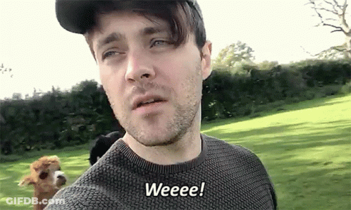 A Man Wearing A Hat And Sweater Says Weeeee While Standing In A Field GIF