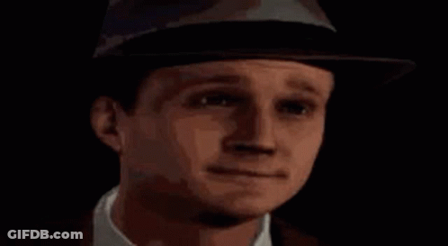 A Man Wearing A Hat And Tie Is Standing In Front Of A Blue X . GIF