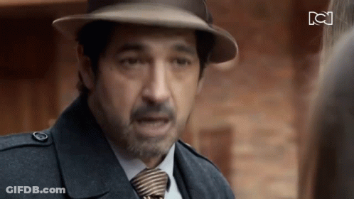 A Man Wearing A Hat And Tie Is Talking To Another Man GIF
