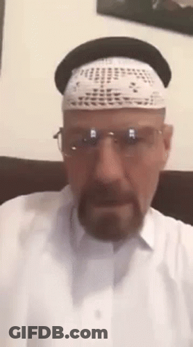 A Man Wearing A Hat , Glasses And A White Shirt Is Sitting On A Couch . GIF