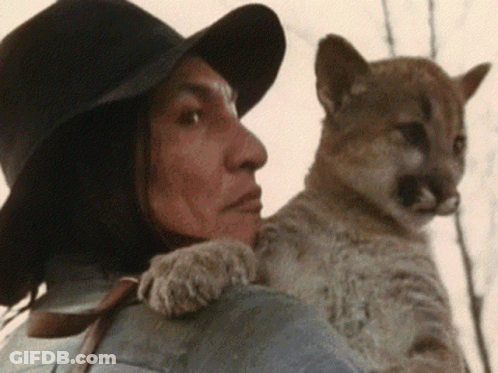 A Man Wearing A Hat Is Holding A Small Animal On His Shoulder GIF
