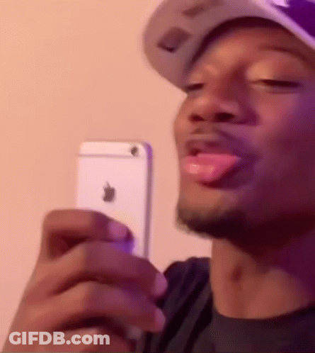 A Man Wearing A Hat Is Holding A White Iphone In His Hand . GIF