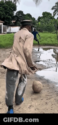 A Man Wearing A Hat Is Kicking A Soccer Ball In A Muddy Field . GIF