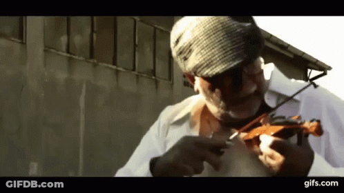A Man Wearing A Hat Is Playing A Violin In Front Of A Building .. GIF