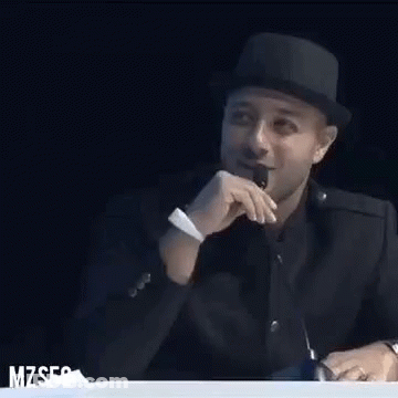 A Man Wearing A Hat Is Sitting At A Table With A Microphone In Front Of Him . GIF