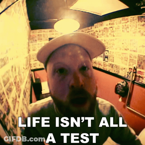 A Man Wearing A Hat Is Sitting In A Bathroom With The Words Life Is N't All A Test Above Him GIF