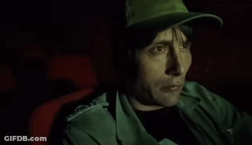 A Man Wearing A Hat Is Sitting In A Dark Room . GIF