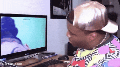 A Man Wearing A Hat Is Sitting In Front Of A Computer Screen GIF