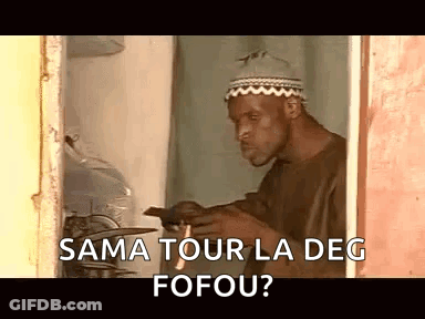 A Man Wearing A Hat Is Standing In A Doorway Looking At A Cell Phone And Smoking A Cigarette . GIF