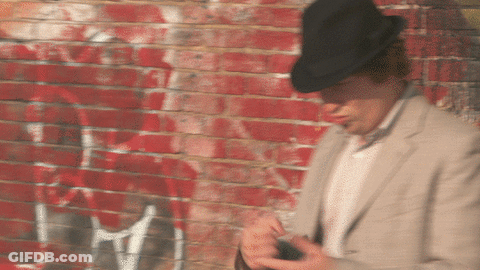 A Man Wearing A Hat Is Standing In Front Of A Brick Wall GIF