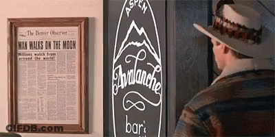 A Man Wearing A Hat Is Standing In Front Of A Sign That Says Avalanche Bar GIF