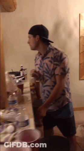 A Man Wearing A Hat Is Standing In Front Of A Table GIF