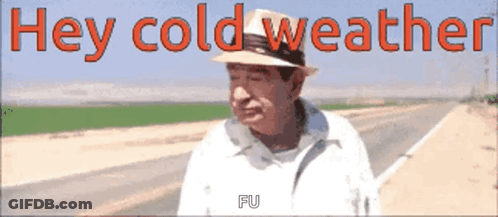 A Man Wearing A Hat Is Standing On The Side Of A Road With The Words Hey Cold Weather Written Above Him GIF