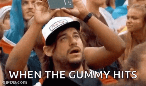 A Man Wearing A Hat Is Taking A Picture Of Himself In A Crowd With The Words When The Gummy Hits . GIF
