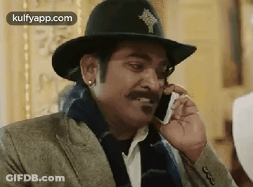 A Man Wearing A Hat Is Talking On A Cell Phone . GIF
