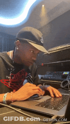 A Man Wearing A Hat Is Typing On A Laptop With Gifrun.com Written On The Bottom Right GIF