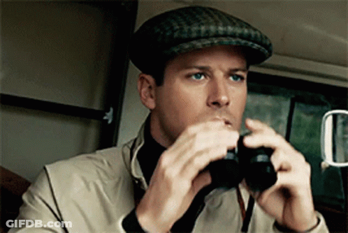 A Man Wearing A Hat Looks Through Binoculars In A Car GIF