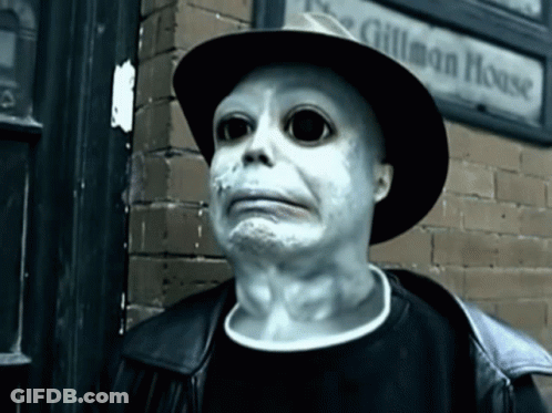 A Man Wearing A Hat Stands In Front Of A Sign That Says Gilman House GIF