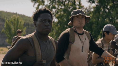 A Man Wearing A Hat Stands Next To Another Man In A Long Walk Advertisement GIF