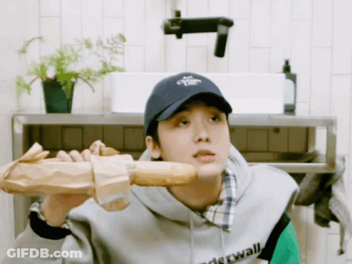 A Man Wearing A Hat That Says " Air " On It Holds A Loaf Of Bread Over His Shoulder GIF
