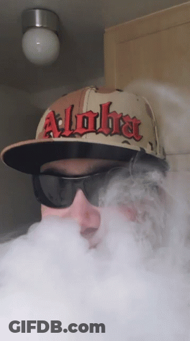 A Man Wearing A Hat That Says Alpha Is Blowing Smoke GIF