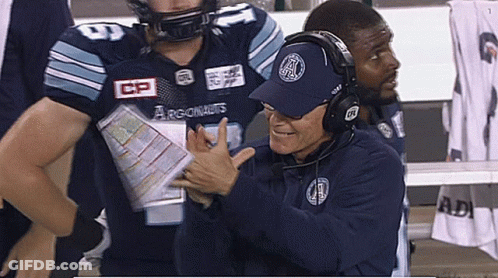A Man Wearing A Hat That Says Argonauts Talks To A Football Player GIF