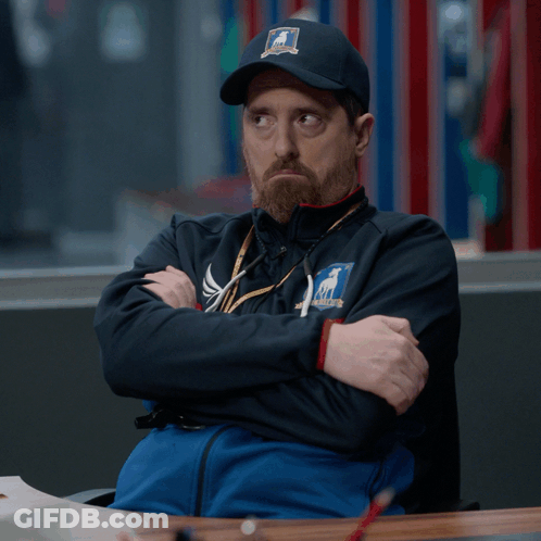 A Man Wearing A Hat That Says ' Chicago ' On It Is Sitting At A Table With His Arms Crossed GIF