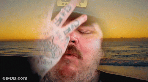A Man Wearing A Hat That Says Cycles Covers His Face With His Hand GIF