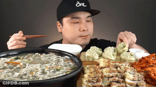 A Man Wearing A Hat That Says Dnt Is Eating Noodles And Meat GIF