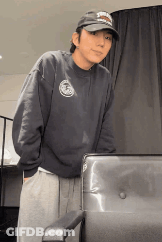 A Man Wearing A Hat That Says ' Harley Davidson ' On It Is Standing Next To A Chair GIF