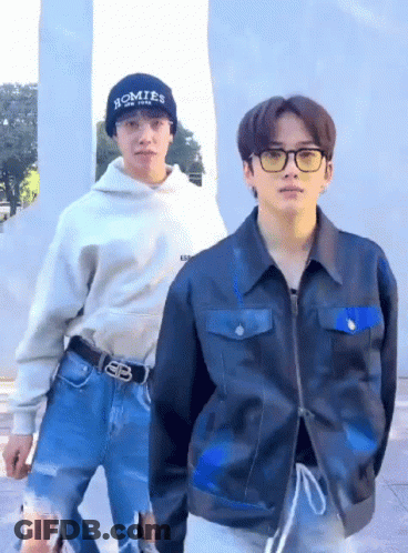 A Man Wearing A Hat That Says Homies On It Is Standing Next To Another Man Wearing A Jacket . GIF