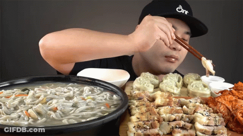 A Man Wearing A Hat That Says One Is Eating Noodles GIF