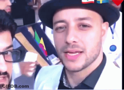 A Man Wearing A Hat With Flags On It Looks At The Camera GIF