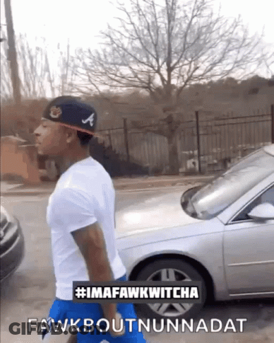 A Man Wearing A Hat With The Letter A On It Is Walking Down A Street GIF